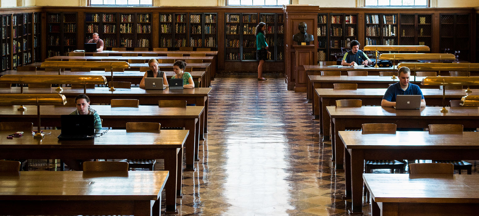 Handful of students sitting at tables in large library hall
