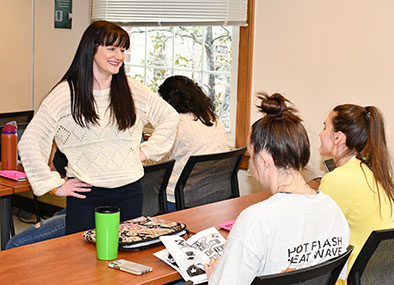 Female professor smiling as she talks to two students seated at a table